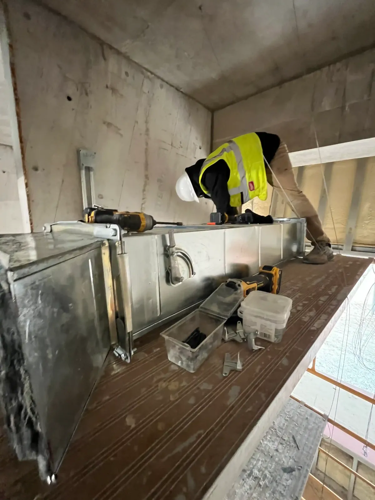 A technician in a high visibility vest working on ductwork in a commercial space