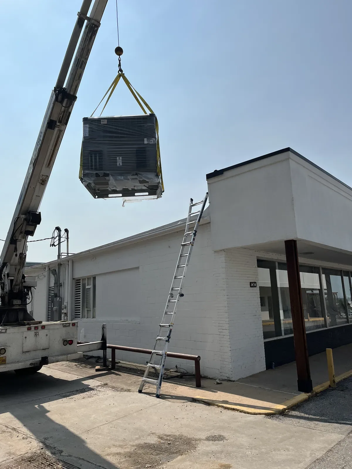 A crane lifting a packaged HVAC unit toward the roof of a single story commercial building