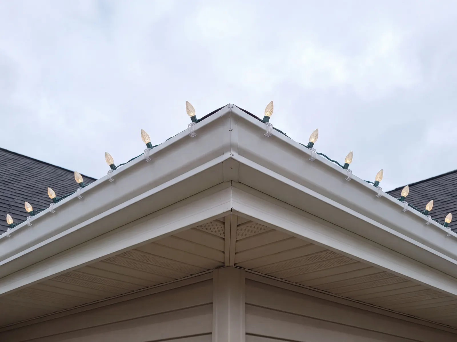 Daytime close-up of C9 bulbs clipped in straight lines along a gutter corner