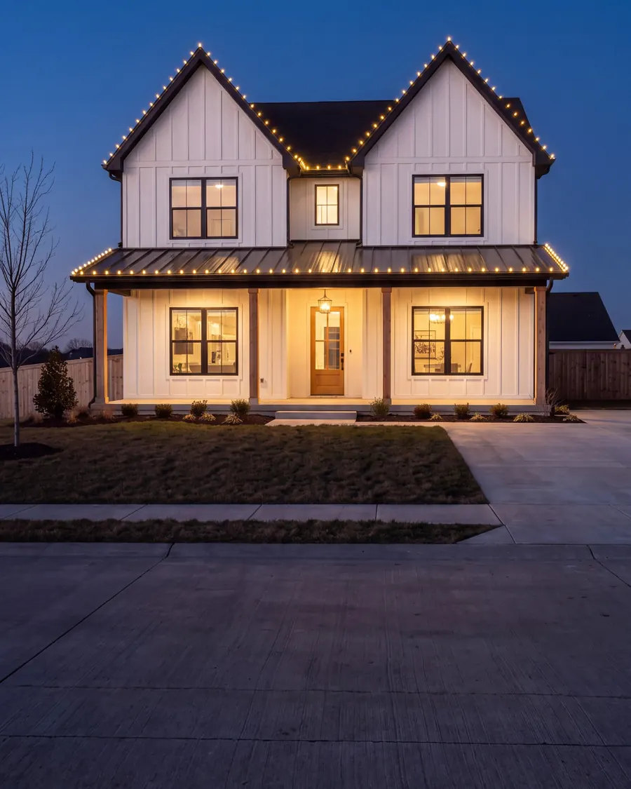 White board-and-batten farmhouse at dusk with warm-white C9 lights along two front gables and the porch roof