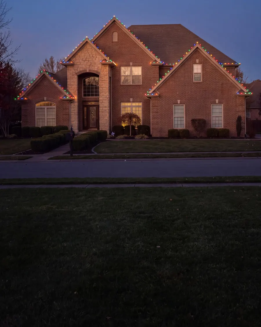 Two-story brick and stone home at dusk with multicolor C9 lights along its gables and eaves
