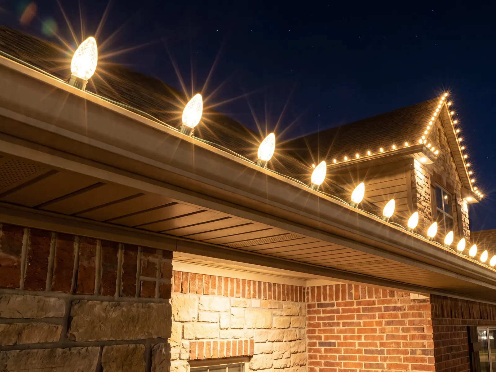 Warm-white C9 bulbs running along the gutter of a stone and brick home at night