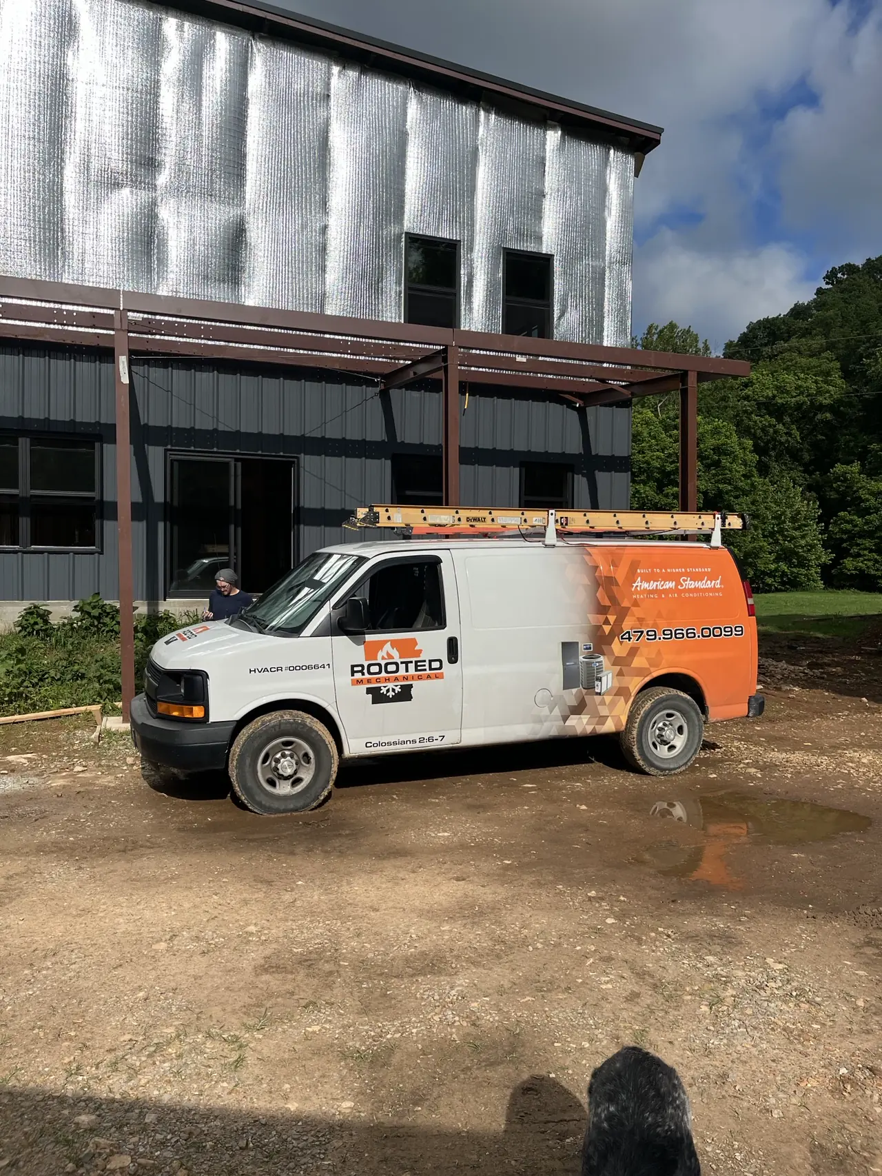 Rooted Mechanical Heating & Air service van with a ladder rack parked at a metal building on a gravel lot