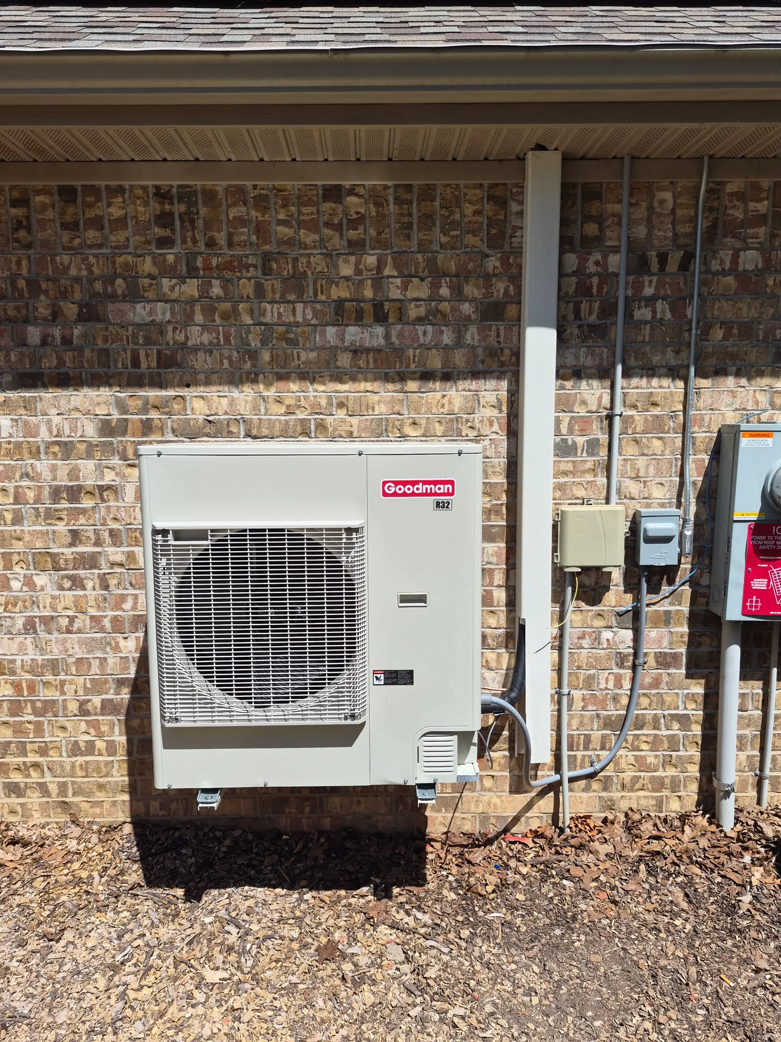 Refrigerant manifold gauges and a clamp meter connected to an outdoor HVAC unit beside a brick home