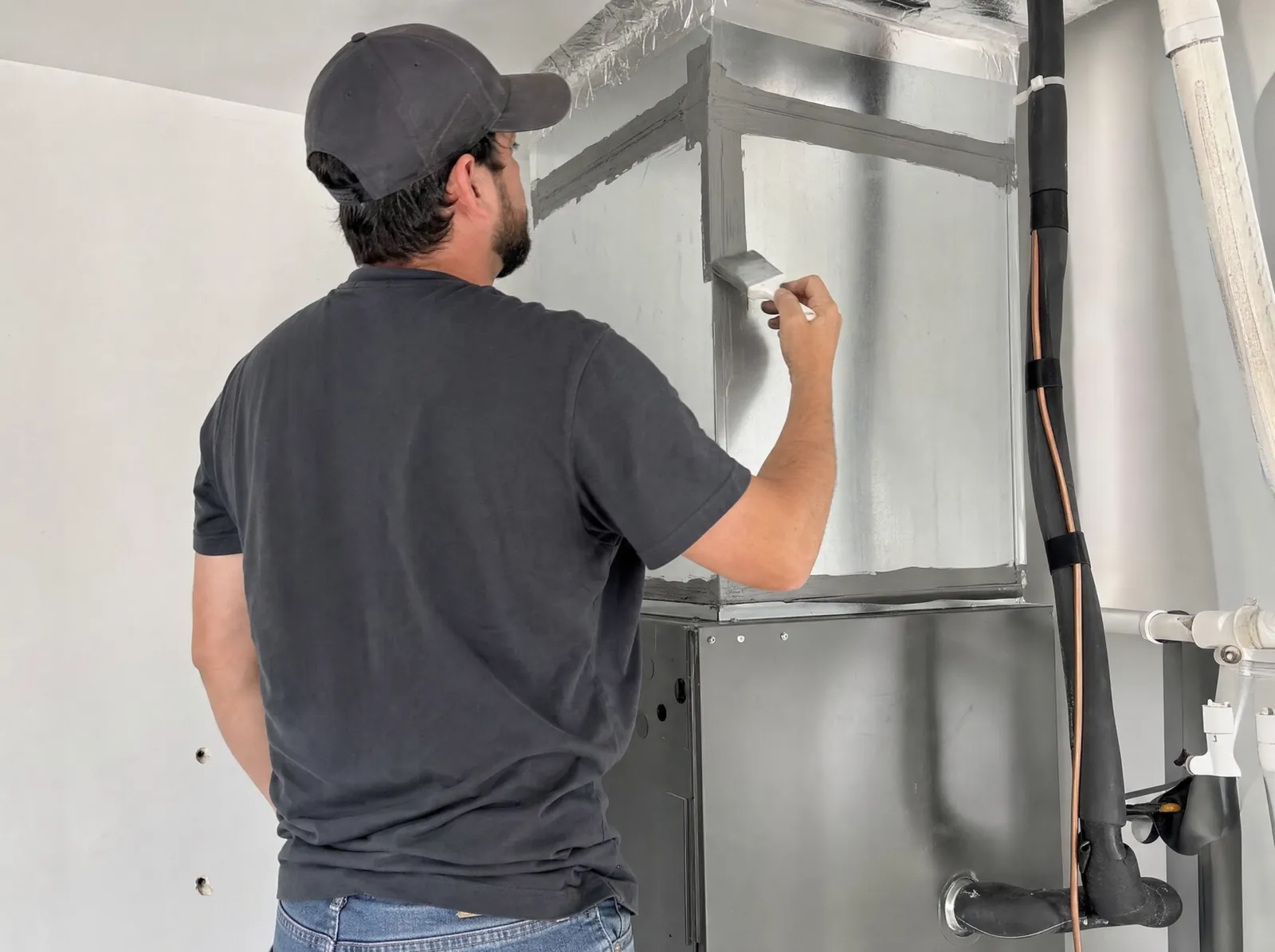 A technician brushes duct mastic over the seams of a sheet metal plenum.