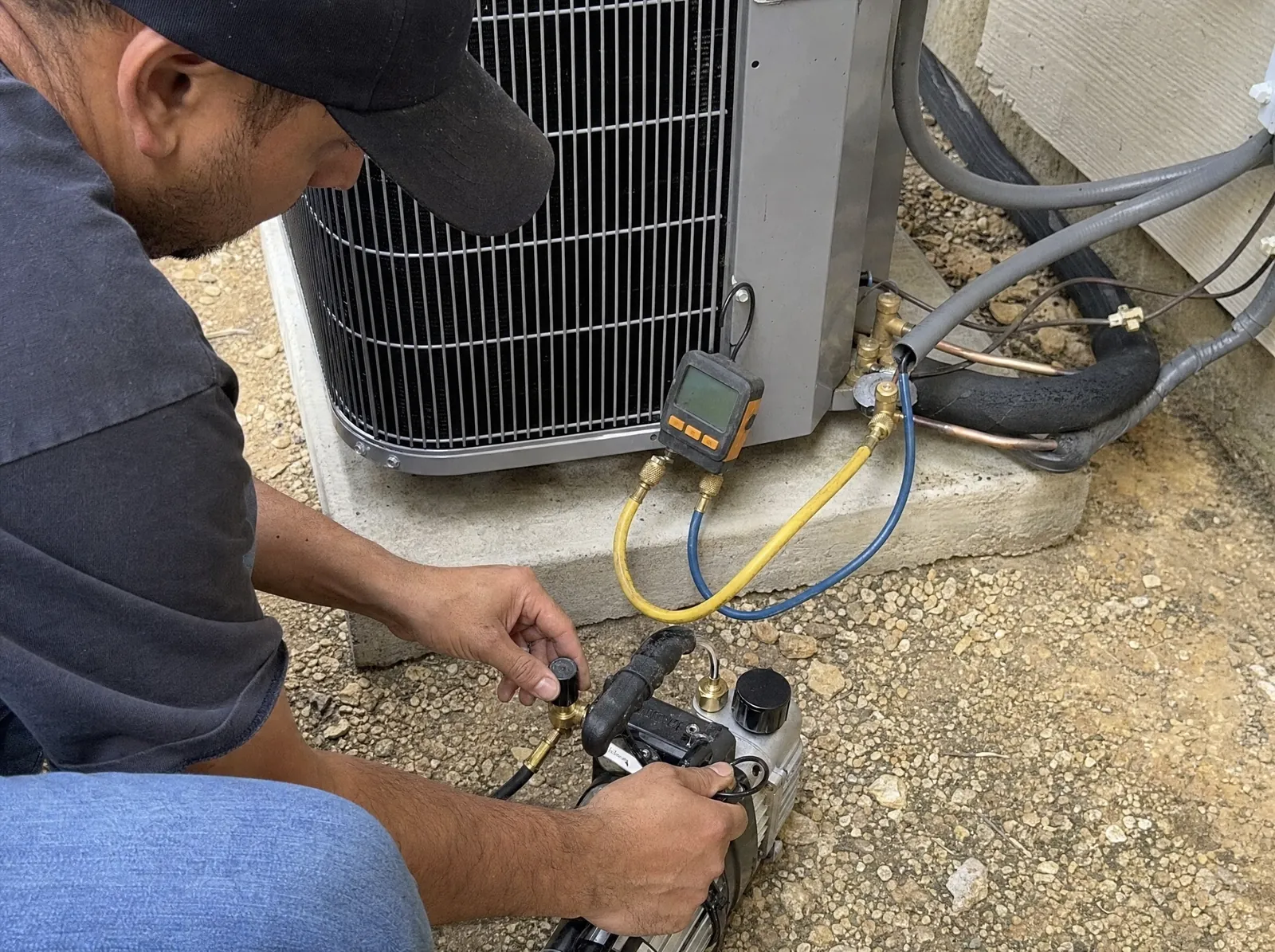 HVAC technician connecting a vacuum pump and a digital micron gauge to the service valves of a new outdoor unit