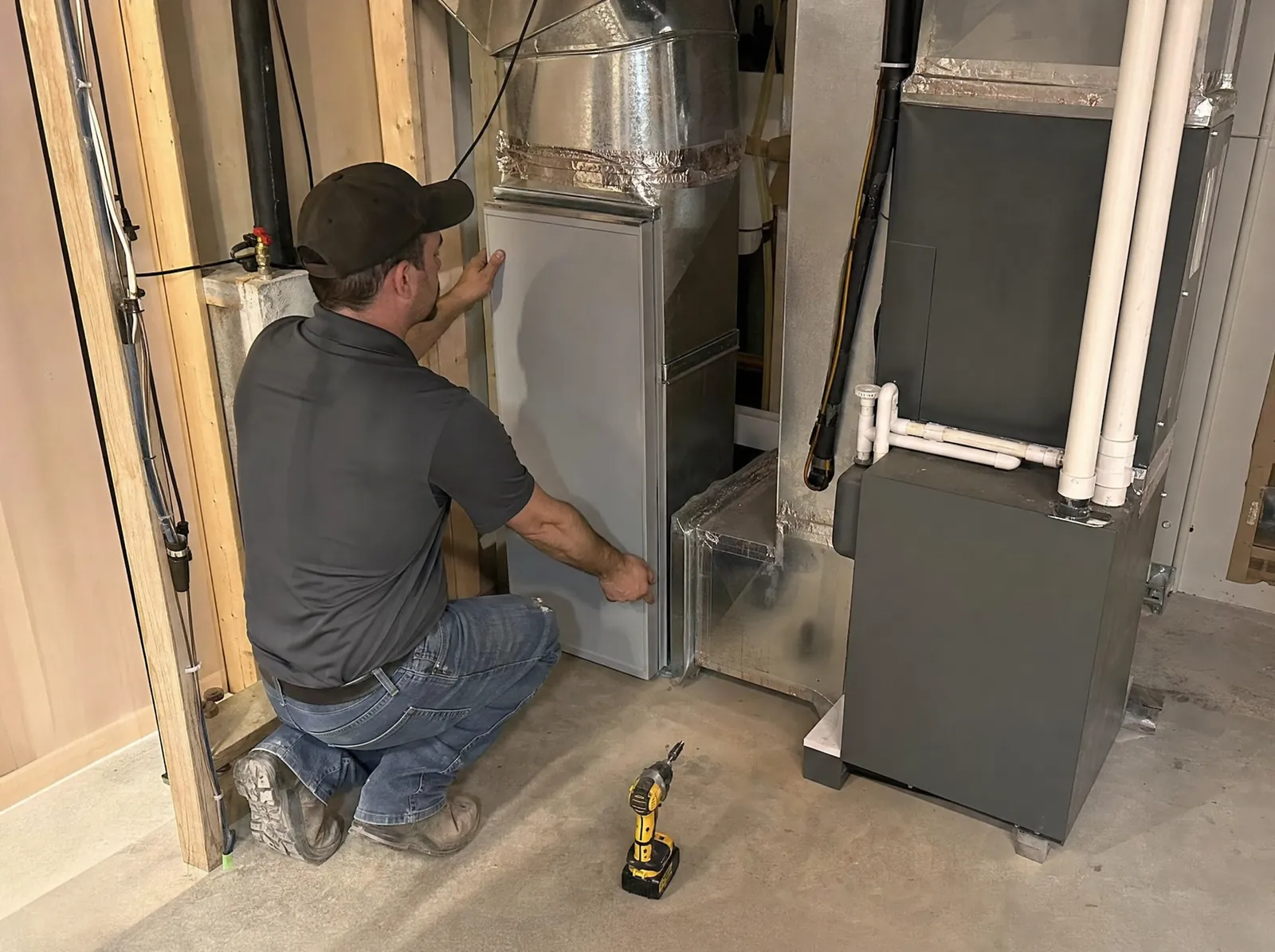 HVAC technician fitting a filter cabinet into the return duct beside a furnace in a basement mechanical room