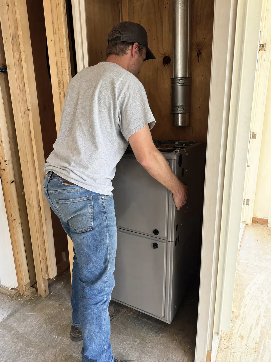 A technician setting a new gas furnace on the floor of a closet, flue not yet connected.
