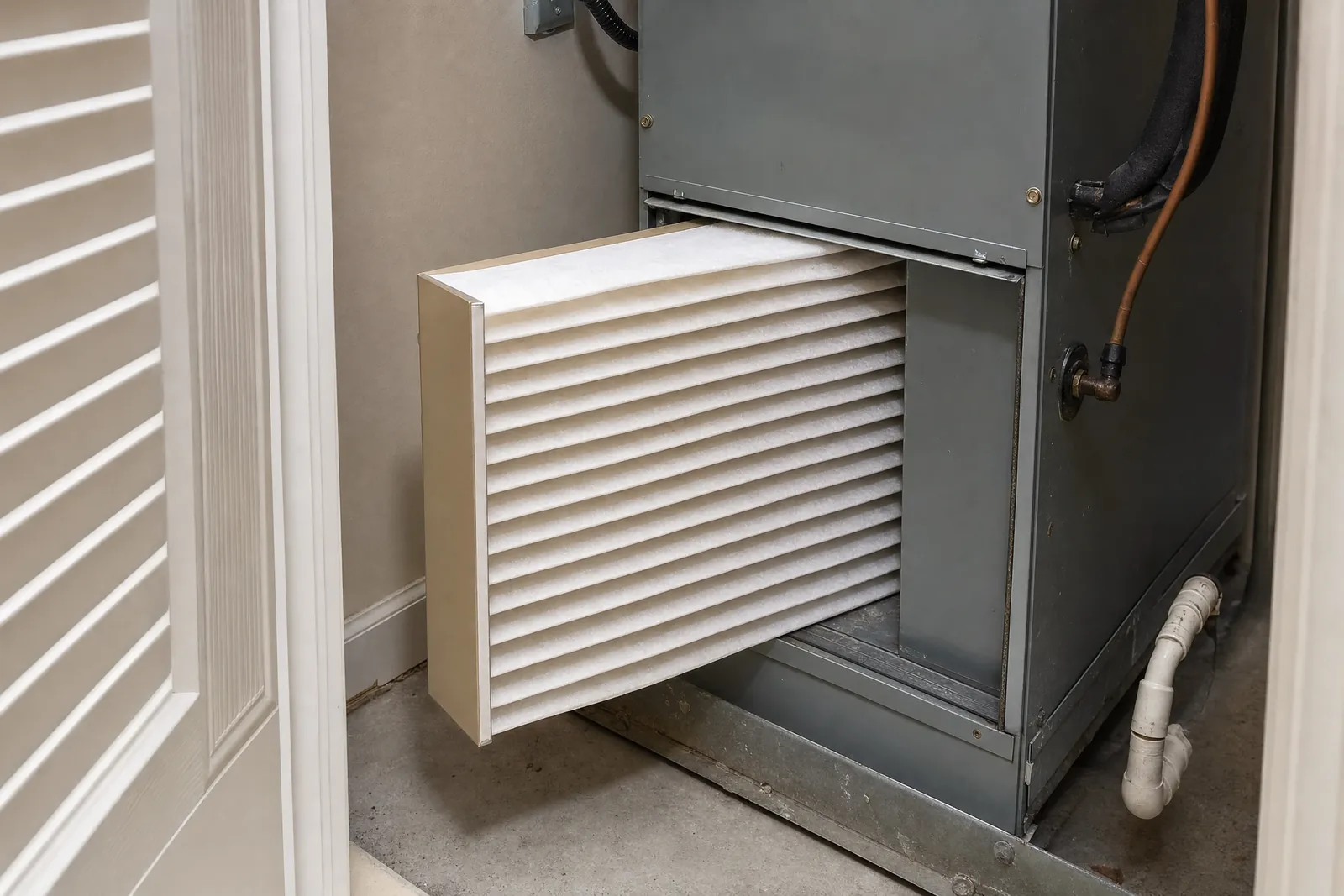 A thick pleated filter half inserted in a sheet-metal filter cabinet.