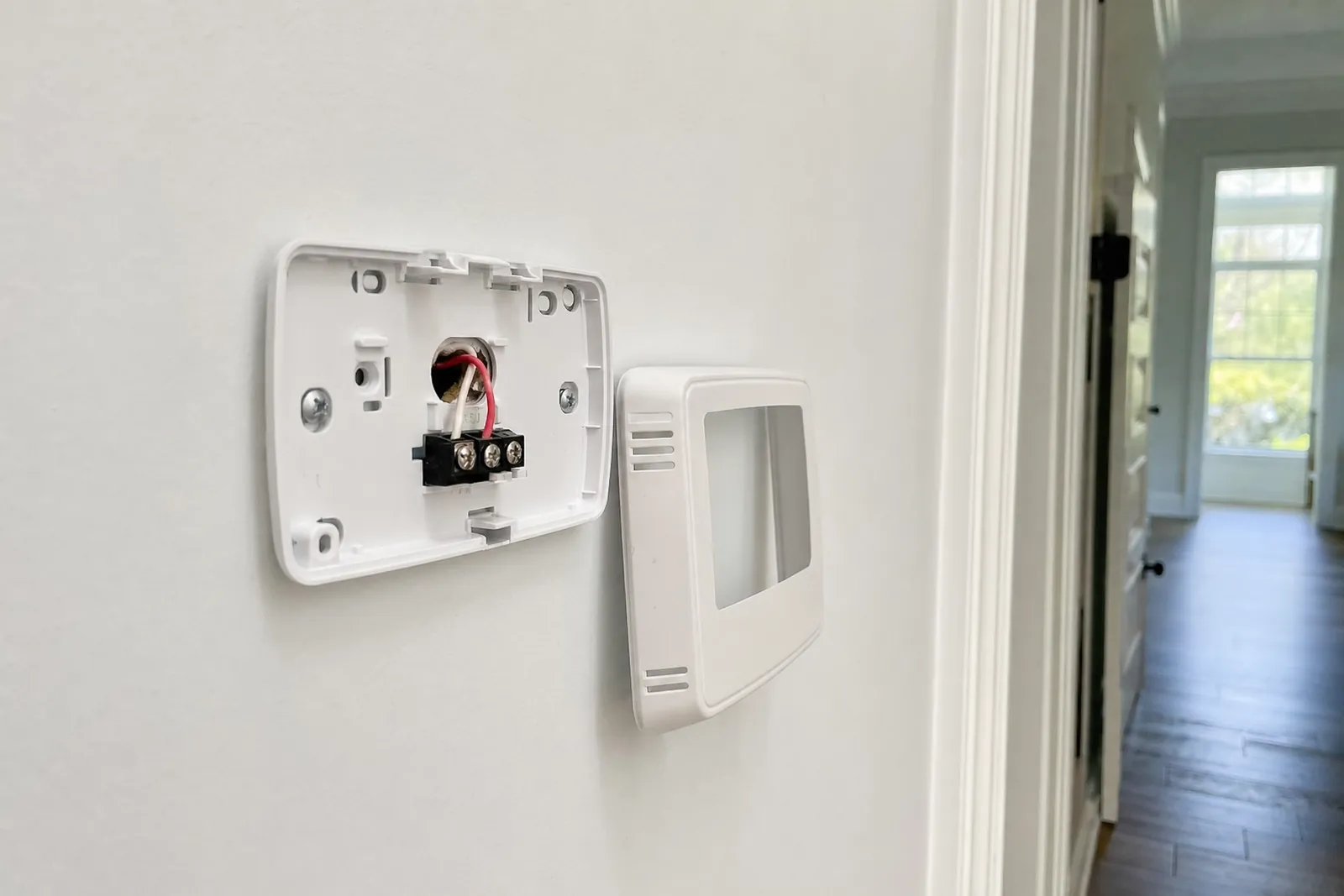 A thermostat base plate on a wall with two low-voltage wires landed, cover set beside it.