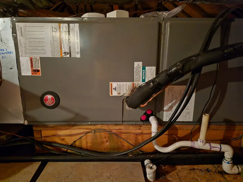 Technician in an orange company shirt installing an outdoor HVAC unit beside a home, with the shipping box nearby