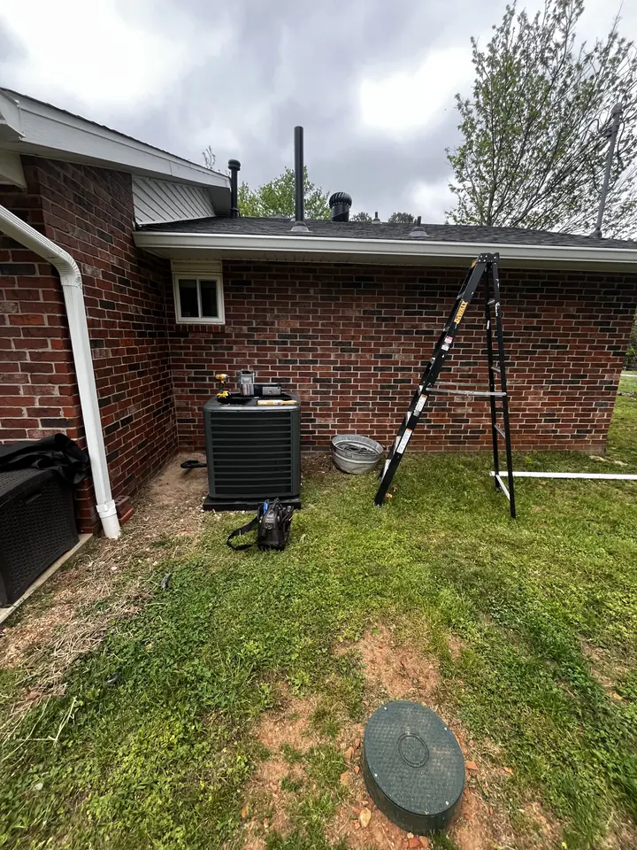 New outdoor HVAC unit on a concrete pad beside a brick home, with a yellow jacket and a level on the ground