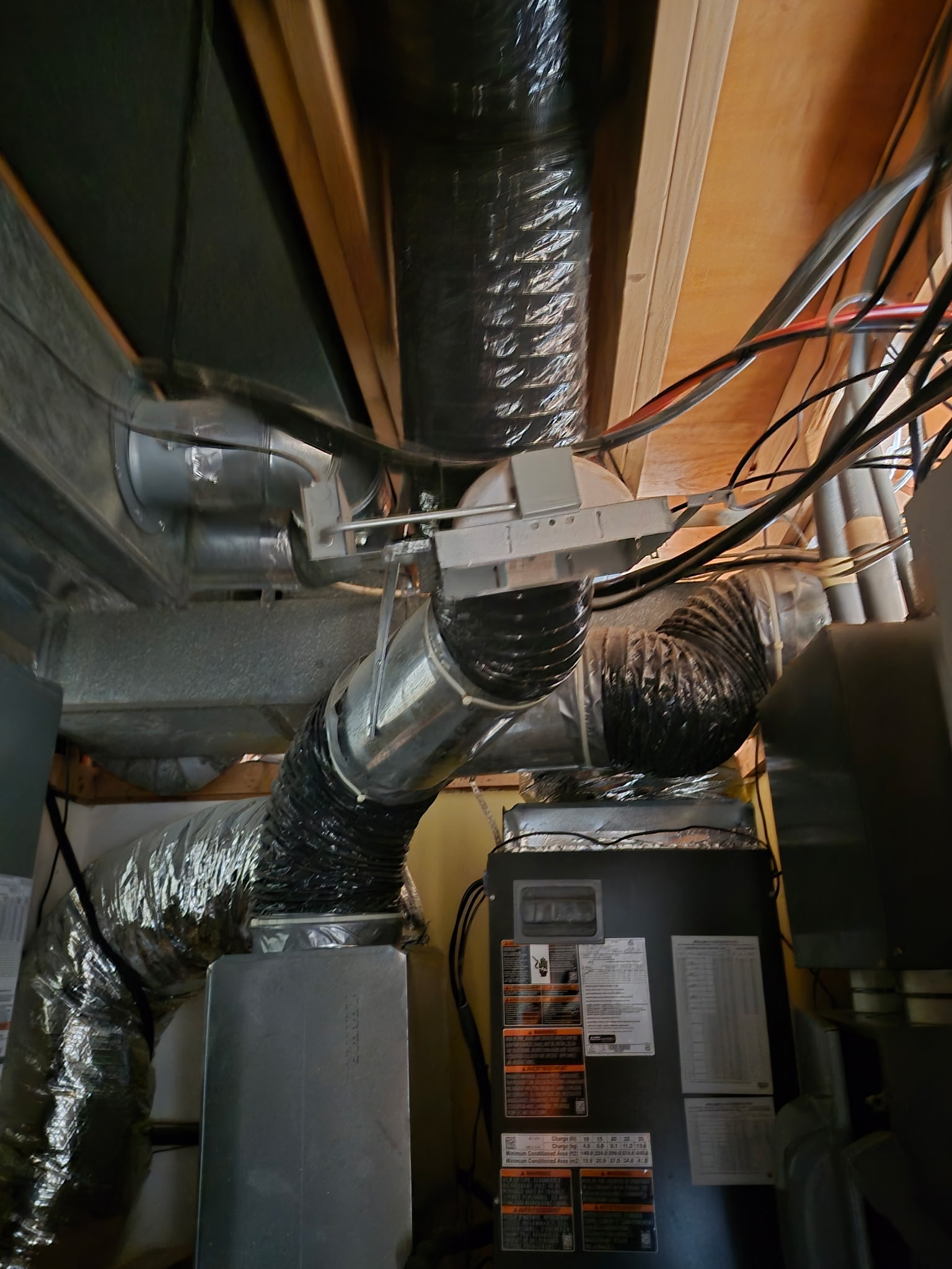Technician in an orange company shirt working inside the open electrical compartment of an outdoor HVAC unit