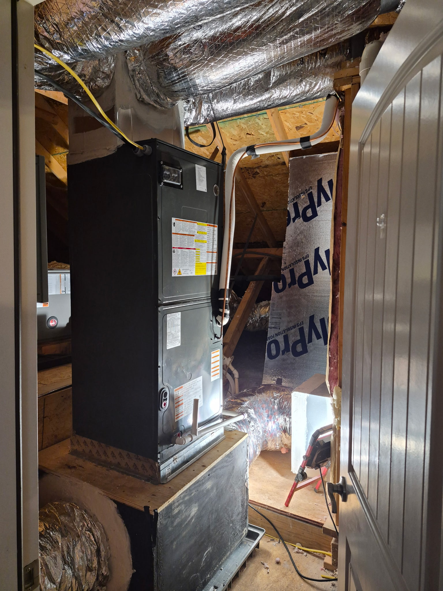 Indoor air handler suspended from floor joists in a crawl space, with flexible duct and a condensate drain